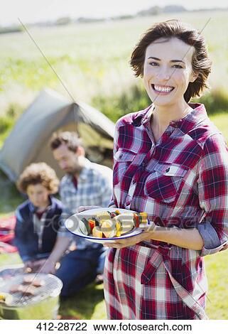 Stock Image - Portrait smiling woman with vegetable skewers at campsite . Fotosearch