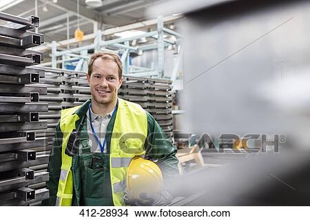 Picture - Portrait smiling worker in protective workwear in steel factory. Fotosearch