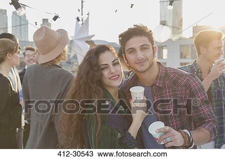 Stock Image - Portrait smiling young couple drinking at rooftop party. Fotosearch