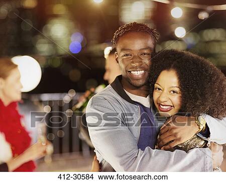 Picture - Portrait smiling young couple hugging at party. Fotosearch