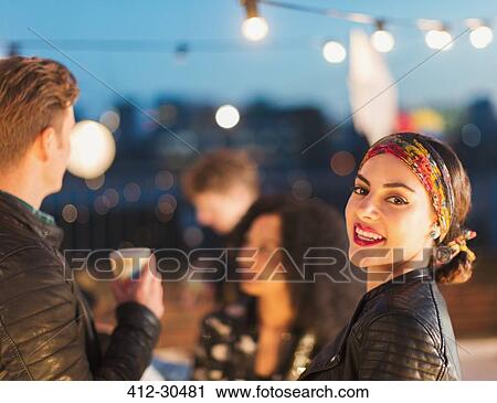 Stock Image - Portrait smiling young woman enjoying rooftop party at night. Fotosearch