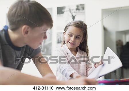 Stock Image - Proud sister showing homework to brother. Fotosearch