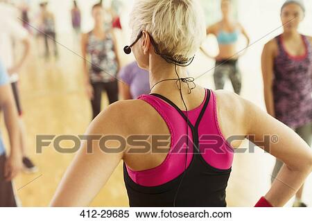 Stock Photography - Rear view fitness instructor with headset leading aerobics class. Fotosearch