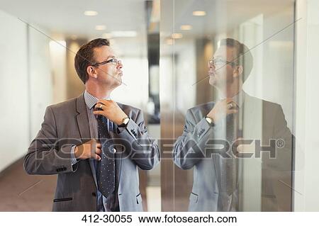 Reflection of confident businessman adjusting tie in office corridor View Large Photo Image Stock Photography - Reflection of confident businessman adjusting tie in office corridor. Fotosearch