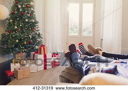 Stock Photo - Relaxed family in socks with feet up near Christmas tree. Fotosearch