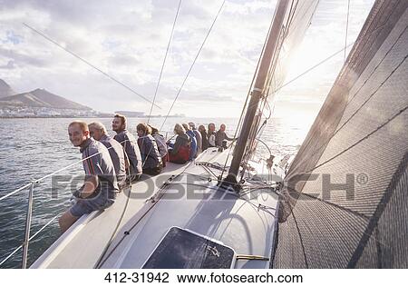 Stock Image - Retired friends sitting on sailboat on sunny ocean. Fotosearch