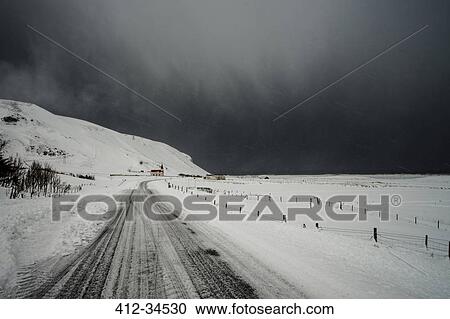 Stock Image - Road through snow covered landscape below stormy sky, Vik, Iceland. Fotosearch