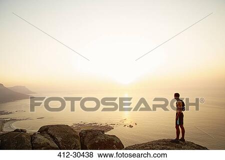 Stock Photo - Runner on rocks looking at sunset ocean view. Fotosearch