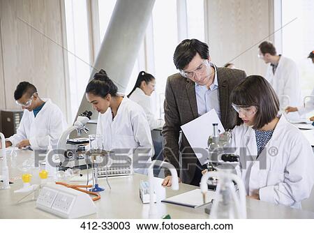 Stock Image - Science professor helping college student conducting scientific experiment in science laboratory classroom. Fotosearch