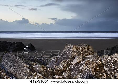 Stock Image - Seascape view behind rocks below overcast sky, Devon, United Kingdom. Fotosearch
