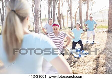 Stock Image - Senior adults practicing yoga in sunny park. Fotosearch
