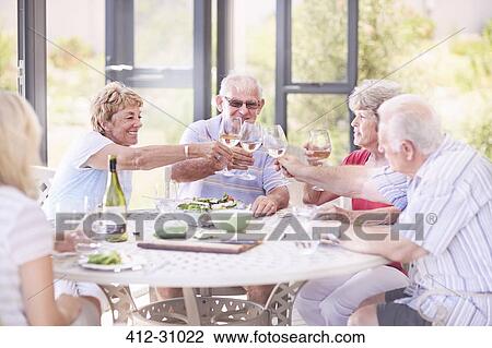 Stock Image - Senior adults toasting wine glasses at patio lunch. Fotosearch