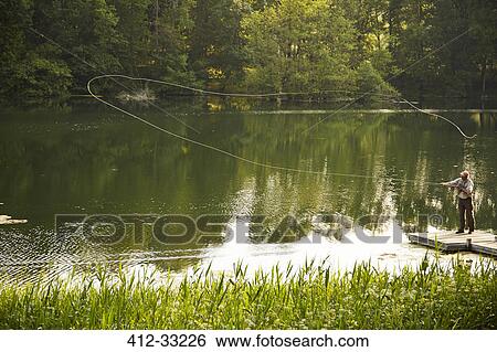 Stock Photograph - Senior man fly fishing on green summer lake. Fotosearch