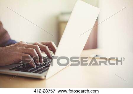 Stock Photo - Senior man typing on laptop at table. Fotosearch