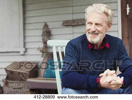 Stock Photo - Senior man with hands clasped looking away on patio. Fotosearch