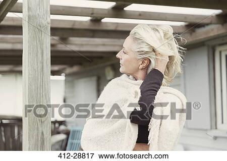 Stock Photo - Senior woman with hand in hair wearing shawl on porch. Fotosearch