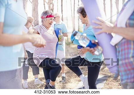 Stock Image - Senior women practicing yoga tree pose in park. Fotosearch