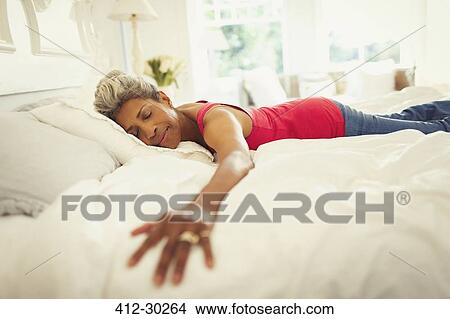 Serene mature woman laying on bed with arms outstretched View Large Photo Image Picture - Serene mature woman laying on bed with arms outstretched. Fotosearch