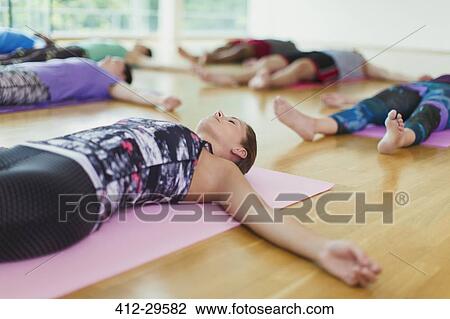 Stock Image - Serene woman in corpse pose in yoga class. Fotosearch
