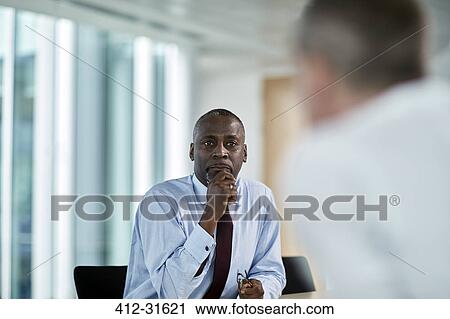 Stock Image - Serious businessman listening to colleague in meeting. Fotosearch