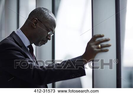 Serious businessman looking down at window View Large Photo Image Stock Image - Serious businessman looking down at window. Fotosearch