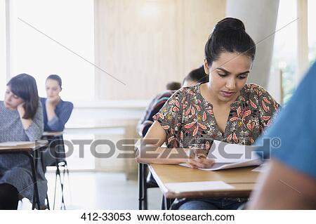 Stock Image - Serious female college student taking test at desk in classroom. Fotosearch