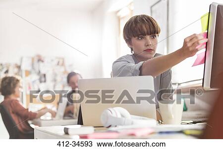 Serious female designer reviewing adhesive notes on computer in office View Large Photo Image Stock Image - Serious female designer reviewing adhesive notes on computer in office. Fotosearch