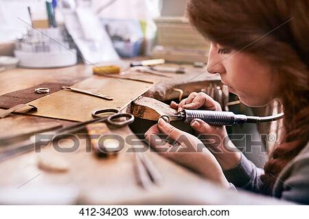 Stock Image - Serious focused female jeweler using equipment in workshop. Fotosearch