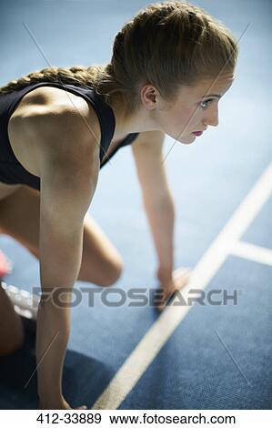 Stock Photo - Serious focused female runner ready at starting block on sports track. Fotosearch