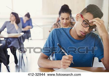 Picture - Serious male college student taking test at desk in classroom. Fotosearch