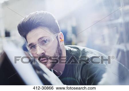 Serious worker examining piece in steel factory View Large Photo Image Stock Photograph - Serious worker examining piece in steel factory. Fotosearch