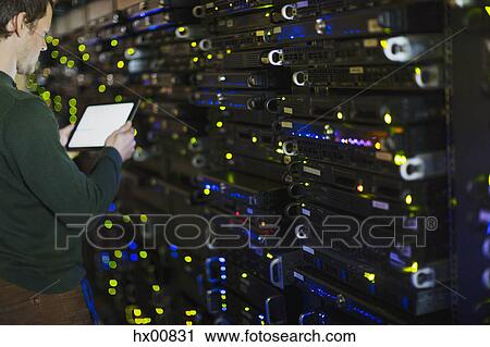 Stock Image - Server room technician using digital tablet at panel. Fotosearch