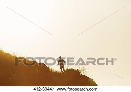 Stock Photo - Silhouette of a man running on hill at sunset. Fotosearch
