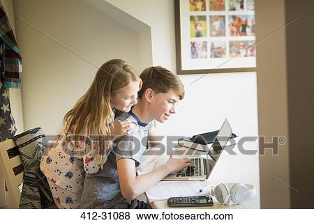Stock Photo - Sister watching brother using laptop in bedroom. Fotosearch
