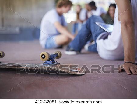 Skateboard upside-down next to teenage friends hanging out at skate park View Large Photo Image Stock Image - Skateboard upside-down next to teenage friends hanging out at skate park. Fotosearch