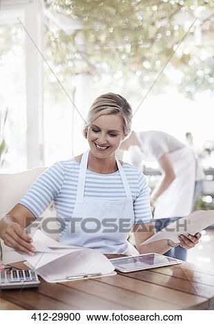 Stock Image - Smiling business owner doing paperwork. Fotosearch