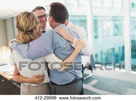 Stock Photo - Smiling business people hugging in huddle in conference room. Fotosearch