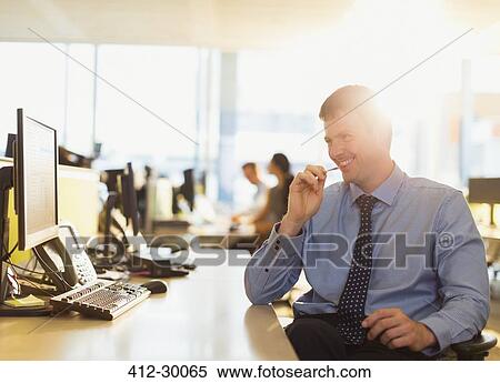 Stock Photography - Smiling businessman at computer in sunny office. Fotosearch
