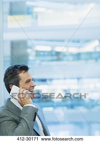 Smiling businessman talking on cell phone in office View Large Photo Image Stock Image - Smiling businessman talking on cell phone in office. Fotosearch