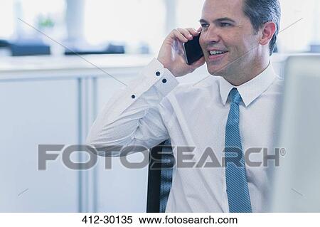 Smiling businessman talking on cell phone in office View Large Photo Image Stock Photography - Smiling businessman talking on cell phone in office. Fotosearch
