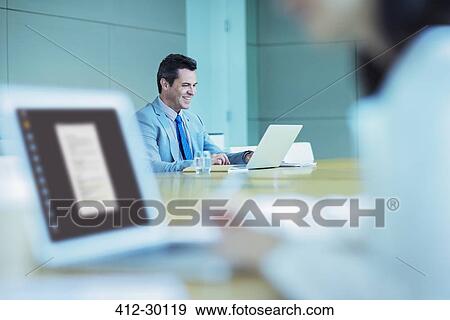 Smiling businessman working at laptop in conference room View Large Photo Image Stock Photo - Smiling businessman working at laptop in conference room. Fotosearch