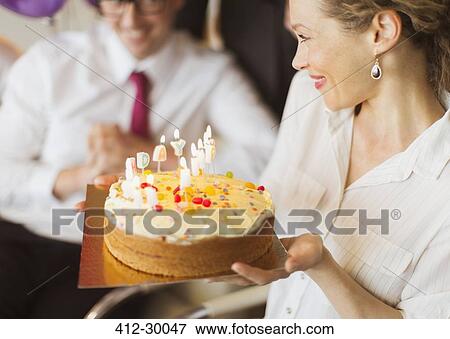 Stock Photo - Smiling businesswoman holding birthday cake with candles. Fotosearch