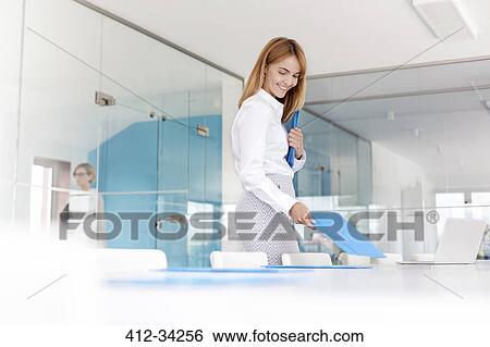 Smiling businesswoman placing folders on conference room table View Large Photo Image Stock Photograph - Smiling businesswoman placing folders on conference room table. Fotosearch