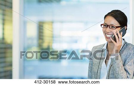 Stock Photo - Smiling businesswoman talking on cell phone in office. Fotosearch