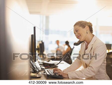 Smiling businesswoman talking on telephone and working at computer in office View Large Photo Image Stock Photo - Smiling businesswoman talking on telephone and working at computer in office. Fotosearch