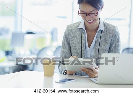 Picture - Smiling businesswoman using digital tablet with coffee in office. Fotosearch