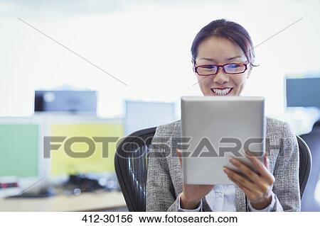 Smiling businesswoman using digital tablet in office View Large Photo Image Stock Photograph - Smiling businesswoman using digital tablet in office. Fotosearch