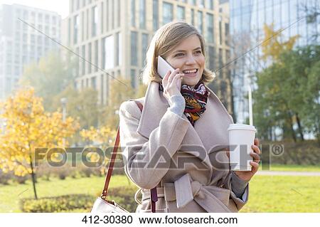 Smiling businesswoman with coffee talking on cell phone in city park View Large Photo Image Stock Image - Smiling businesswoman with coffee talking on cell phone in city park. Fotosearch
