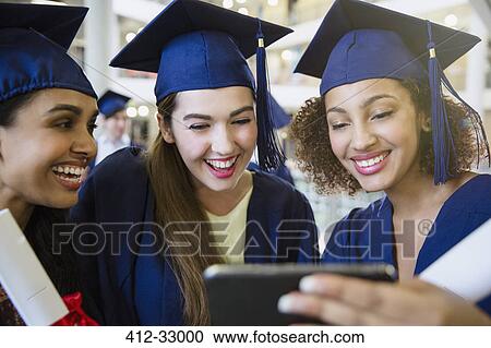 Smiling college graduates in cap and gown using cell phone View Large Photo Image Stock Image - Smiling college graduates in cap and gown using cell phone. Fotosearch
