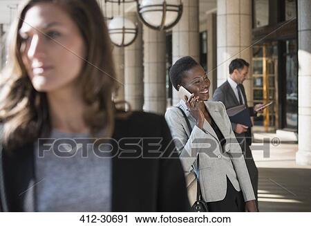 Stock Image - Smiling corporate businesswoman talking on cell phone outside building. Fotosearch